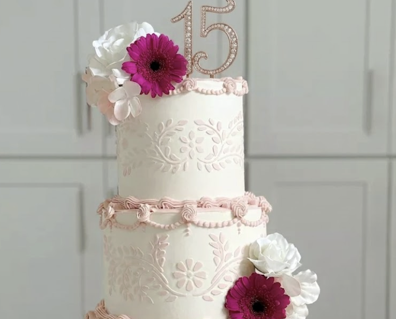 custom three-tier quinceañera cake with pink lace piping, fresh flowers, and rose gold 15 topper
