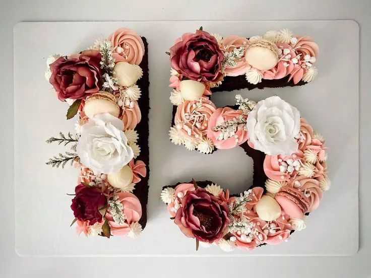 number 15 quinceañera cake decorated with pink and burgundy flowers, macarons, and cream rosettes