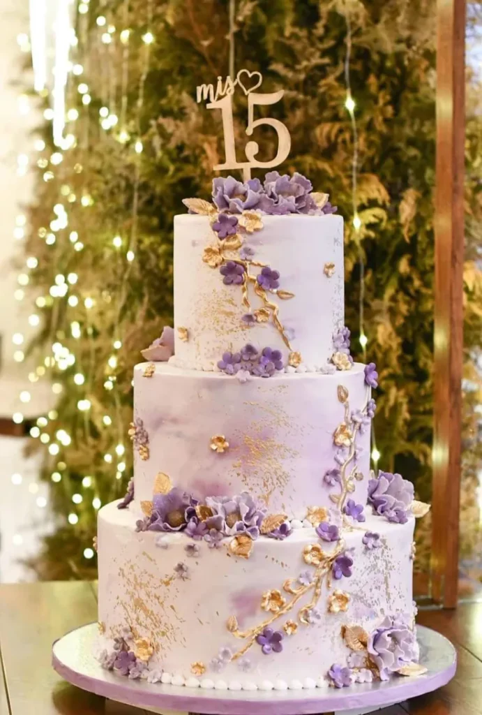 Sweet Fiesta Cakes three-tier quinceañera cake with purple sugar flowers, gold leaf accents, and mis 15 wooden topper